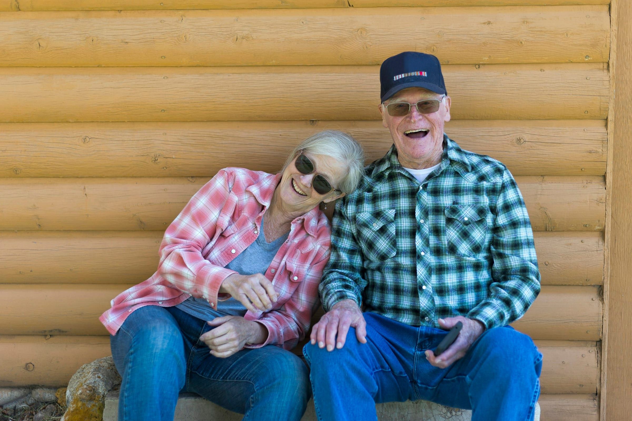 An older couple laughing together on a wooden bench.