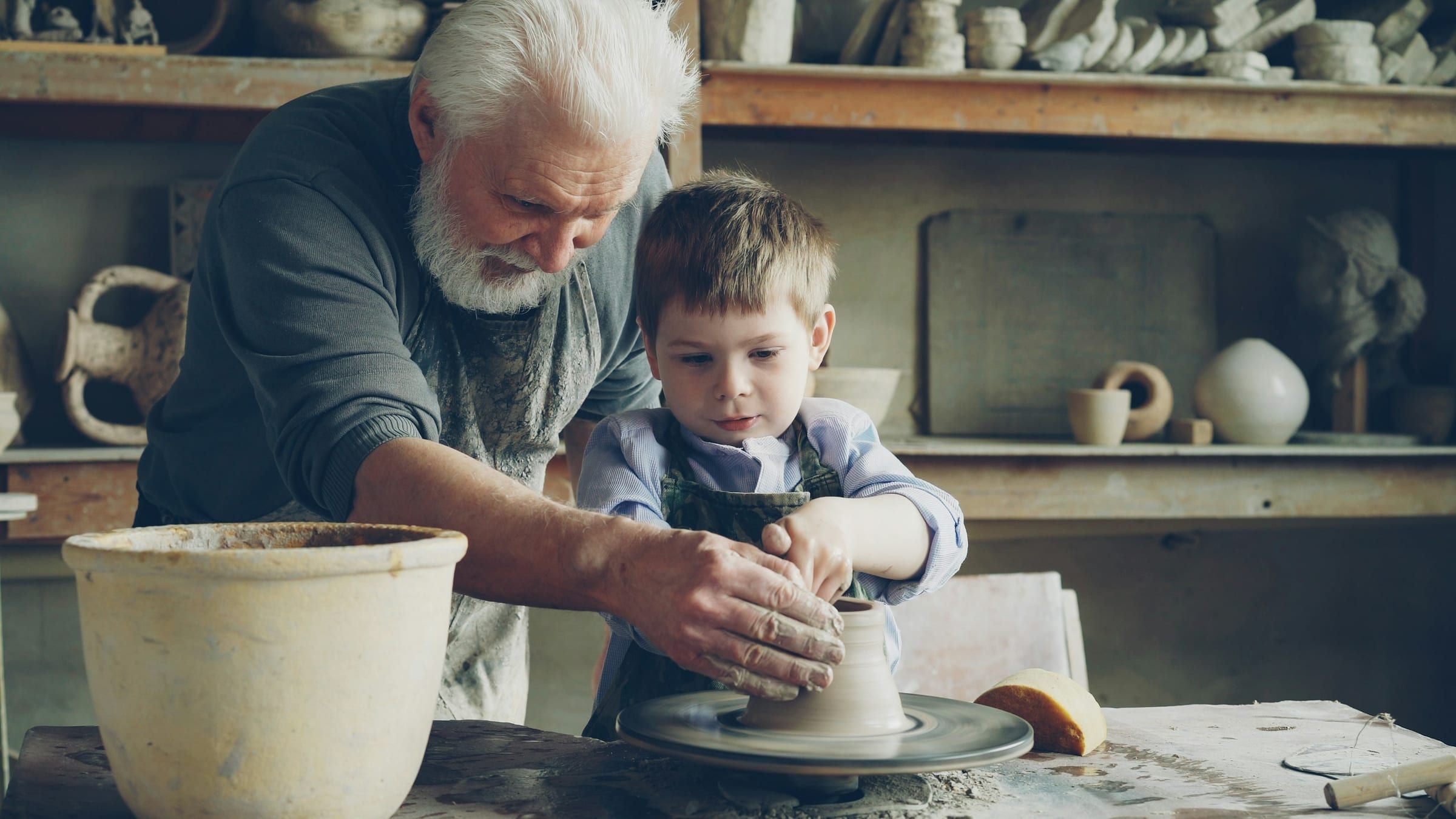 A grandfather's hands guiding his grandson's on a potter's wheel.